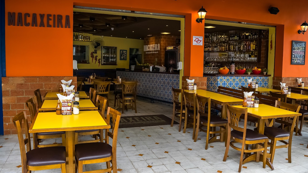 Interior do restaurante Macaxeira com mesas amarelas, decoração com azulejos portugueses e ambiente acolhedor inspirado no Nordeste.