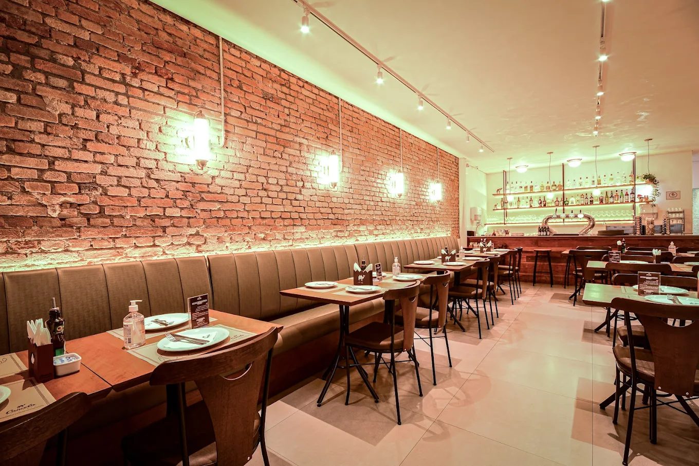 Interior da Pizzaria Camelo Tatuapé com parede de tijolos à vista, bancos estofados marrons e iluminação aconchegante.