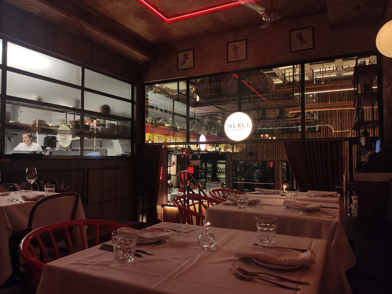 Interior do restaurante Mercie Brasserie com iluminação intimista, mesas arrumadas com toalhas brancas e cadeiras vermelhas.